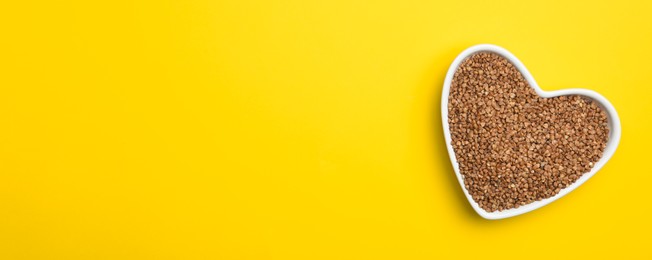 Buckwheat grains on yellow background, top view with space for text. Banner design