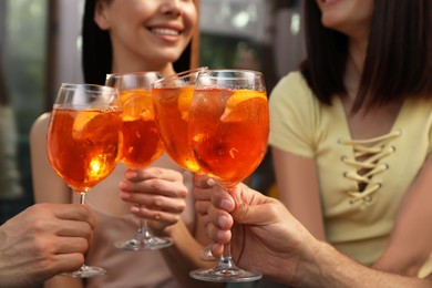 Photo of Friends clinking glasses of Aperol spritz cocktails outdoors, closeup