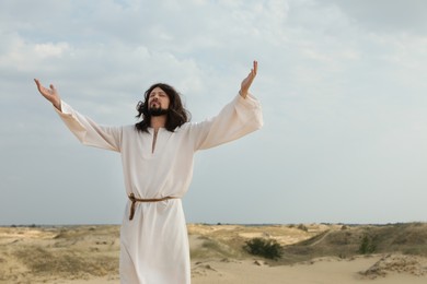 Photo of Jesus Christ raising hands in desert on sunny day