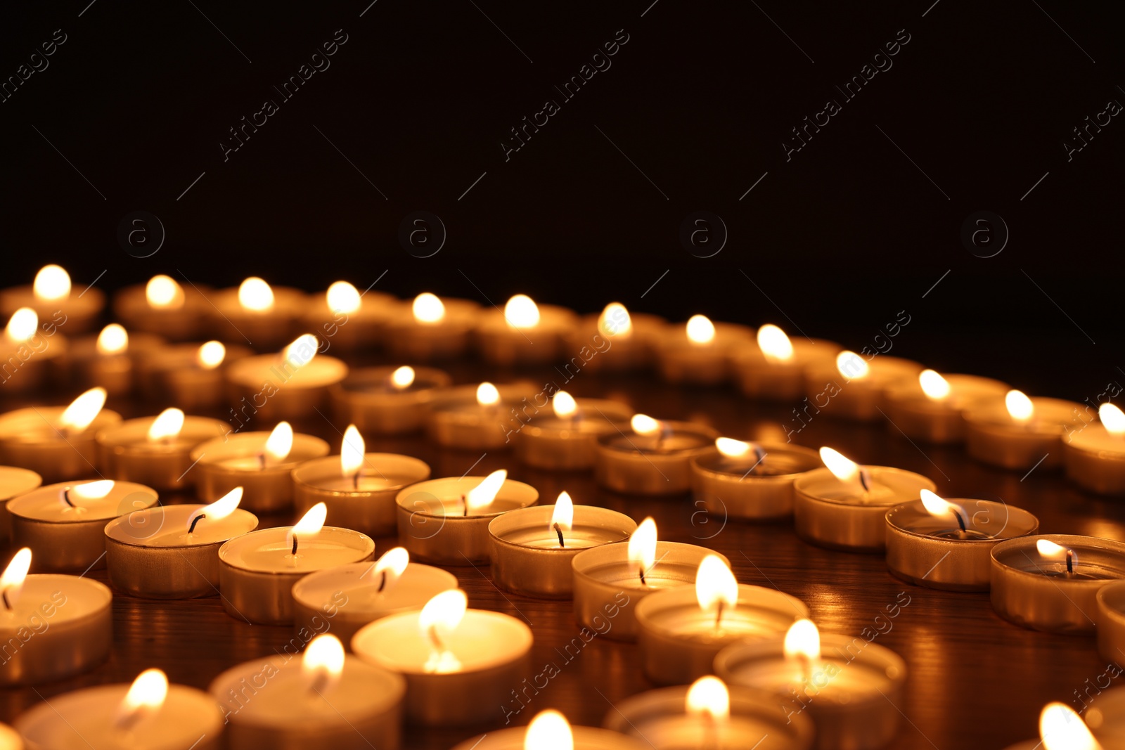 Photo of Burning candles on wooden table against black background