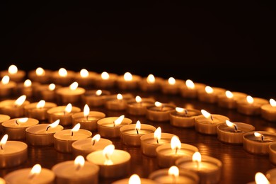 Burning candles on wooden table against black background