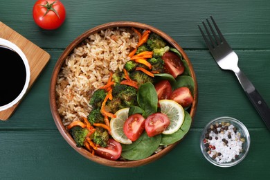 Tasty fried rice with vegetables served on green wooden table, flat lay