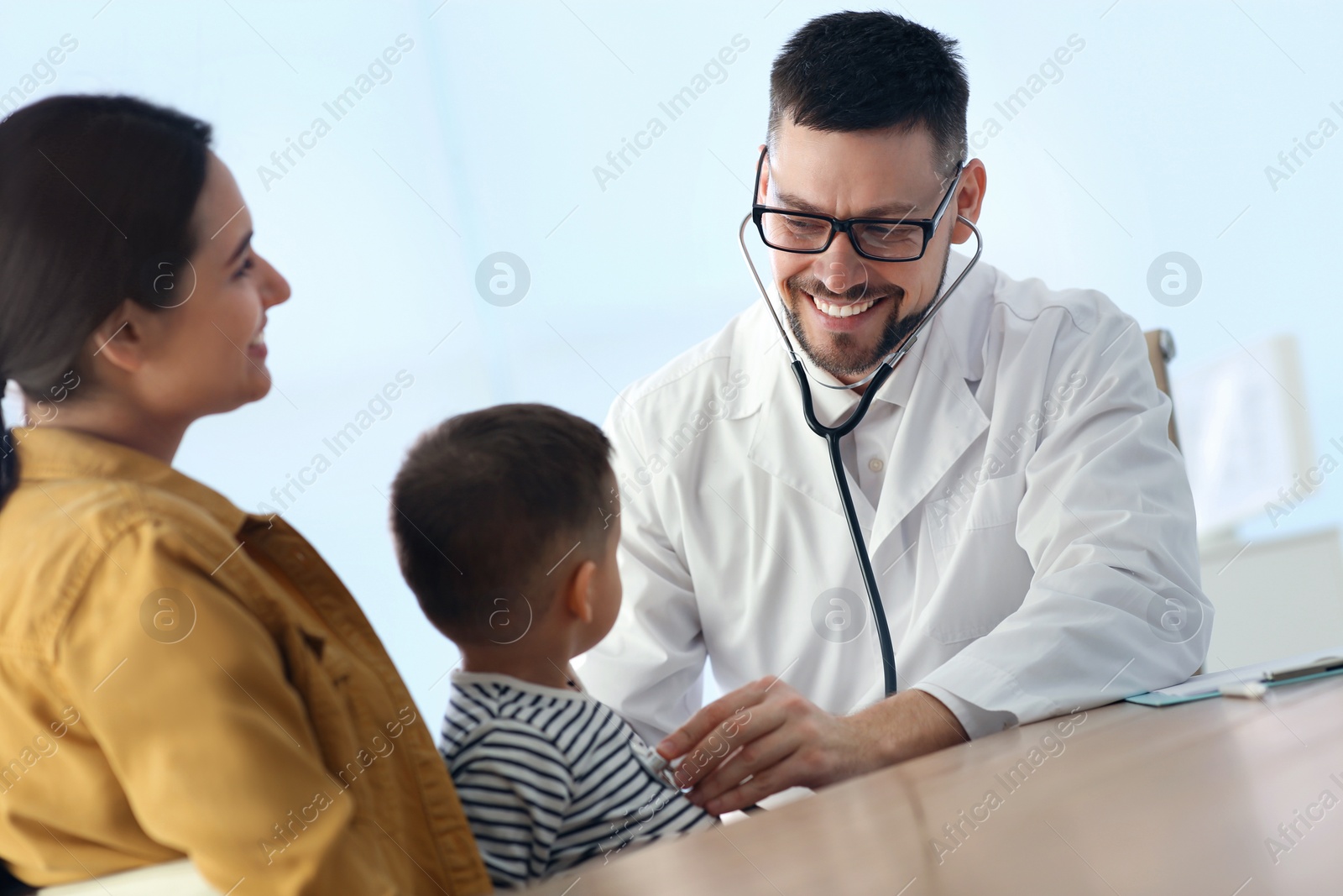 Photo of Mother and son visiting pediatrician in hospital. Doctor examining little boy