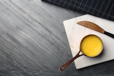 Photo of Stone board with saucepan of clarified butter and knife on table, flat lay. Space for text