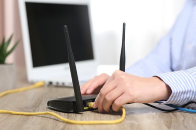 Photo of Woman inserting ethernet cable into Wi-Fi router at wooden table indoors, closeup