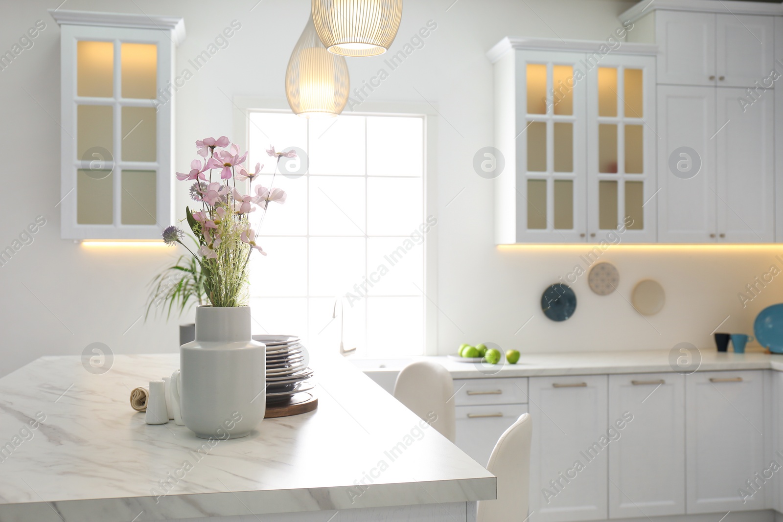 Photo of Beautiful flowers and dishware on white marble table in modern kitchen