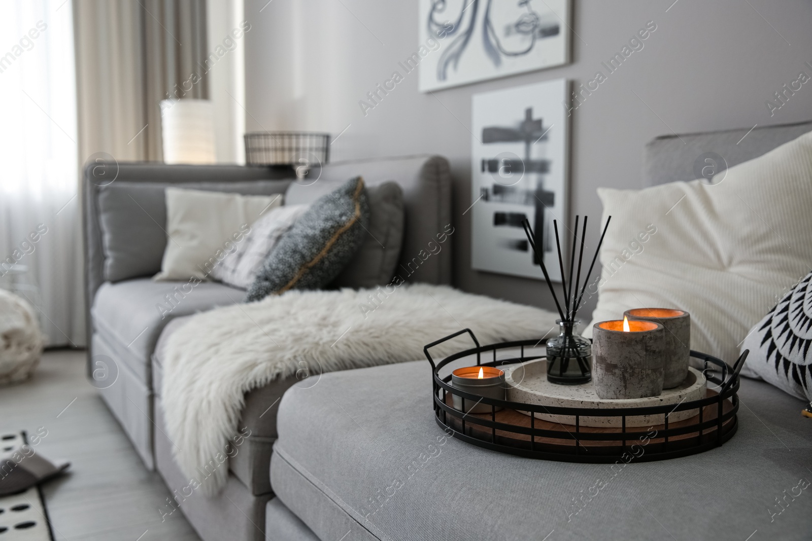 Photo of Candles and aroma reed diffuser on grey sofa, space for text