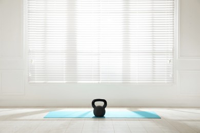 Photo of Exercise mat with kettlebell near window in spacious room