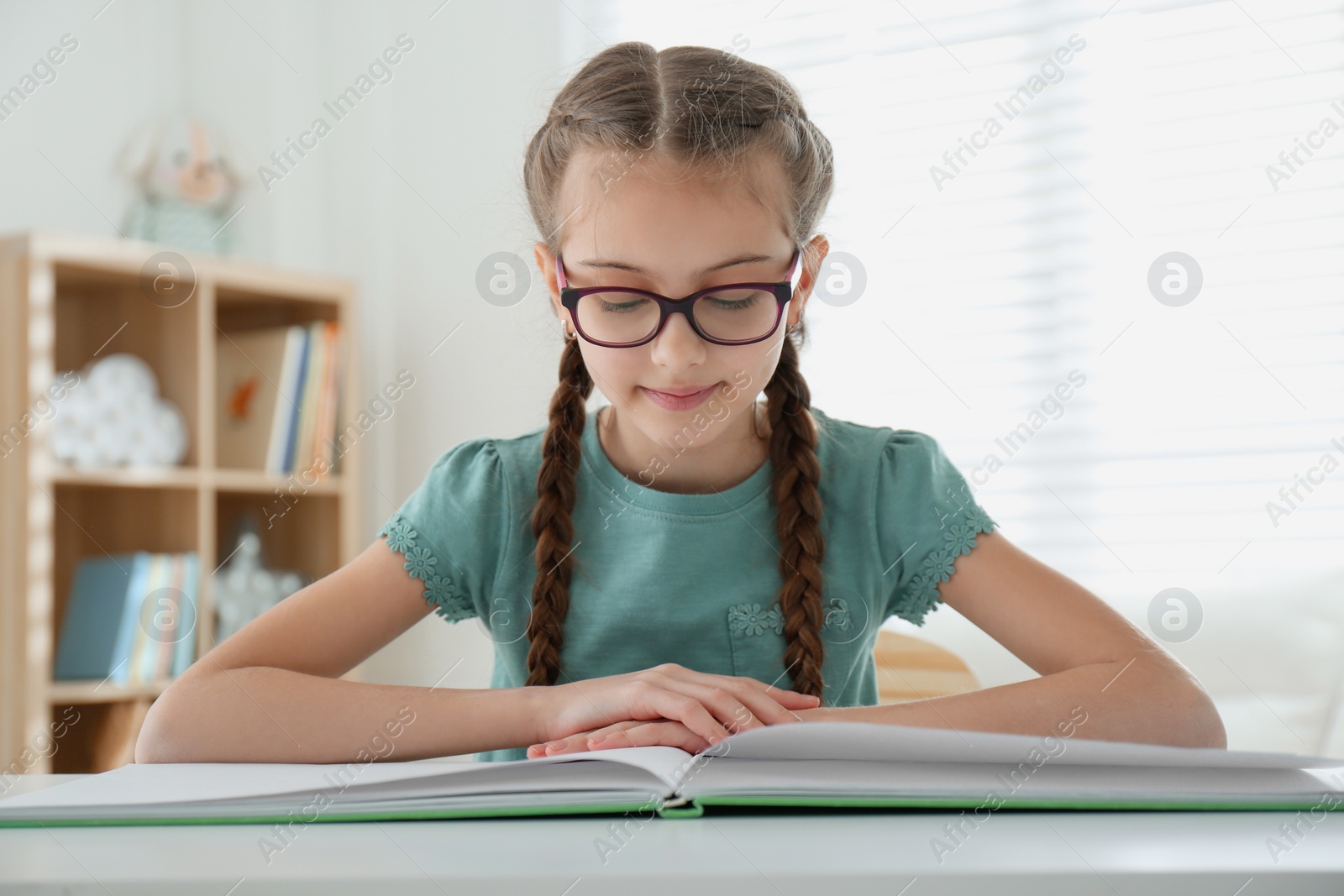 Photo of Cute little girl reading book at desk in room