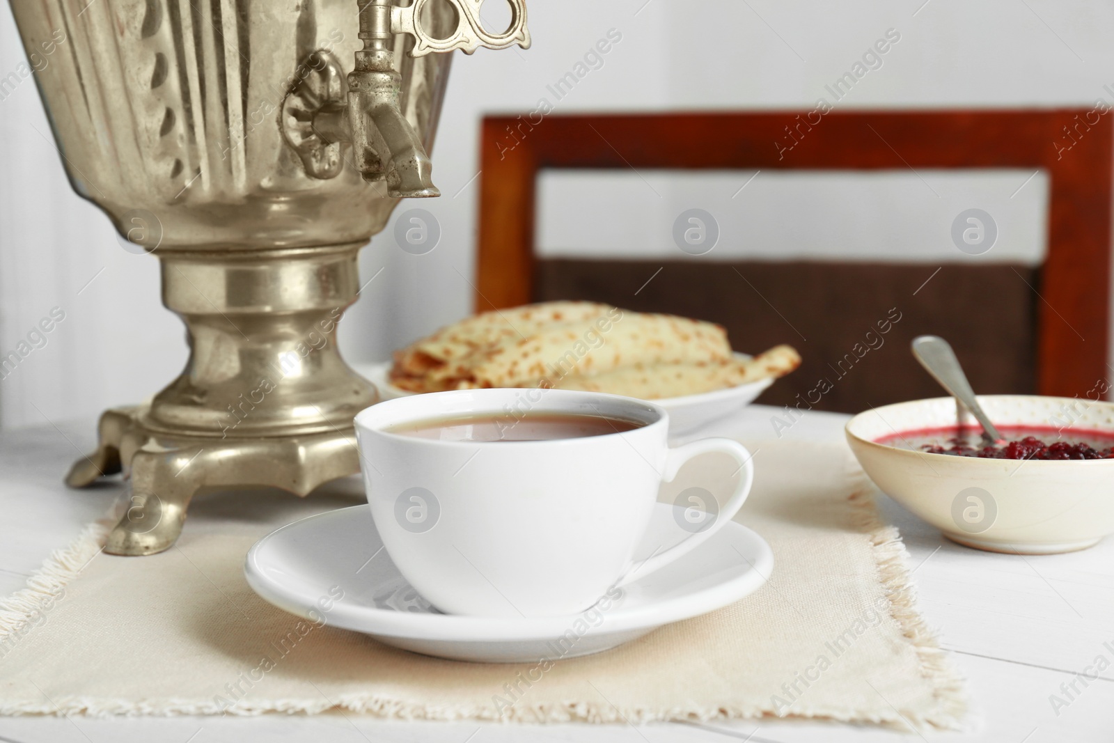 Photo of Vintage samovar, cup of hot drink and snacks served on white wooden table. Traditional Russian tea ceremony