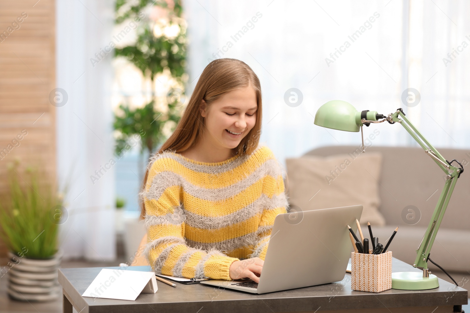 Photo of Pretty teenage girl using laptop at table in room
