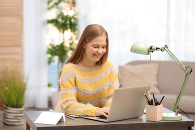 Pretty teenage girl using laptop at table in room