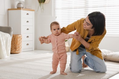 Photo of Mother supporting her baby daughter while she learning to walk at home. Space for text