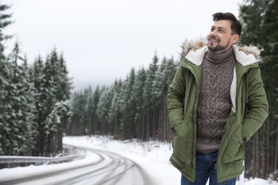Photo of Man in warm clothes near snowy forest, space for text. Winter vacation