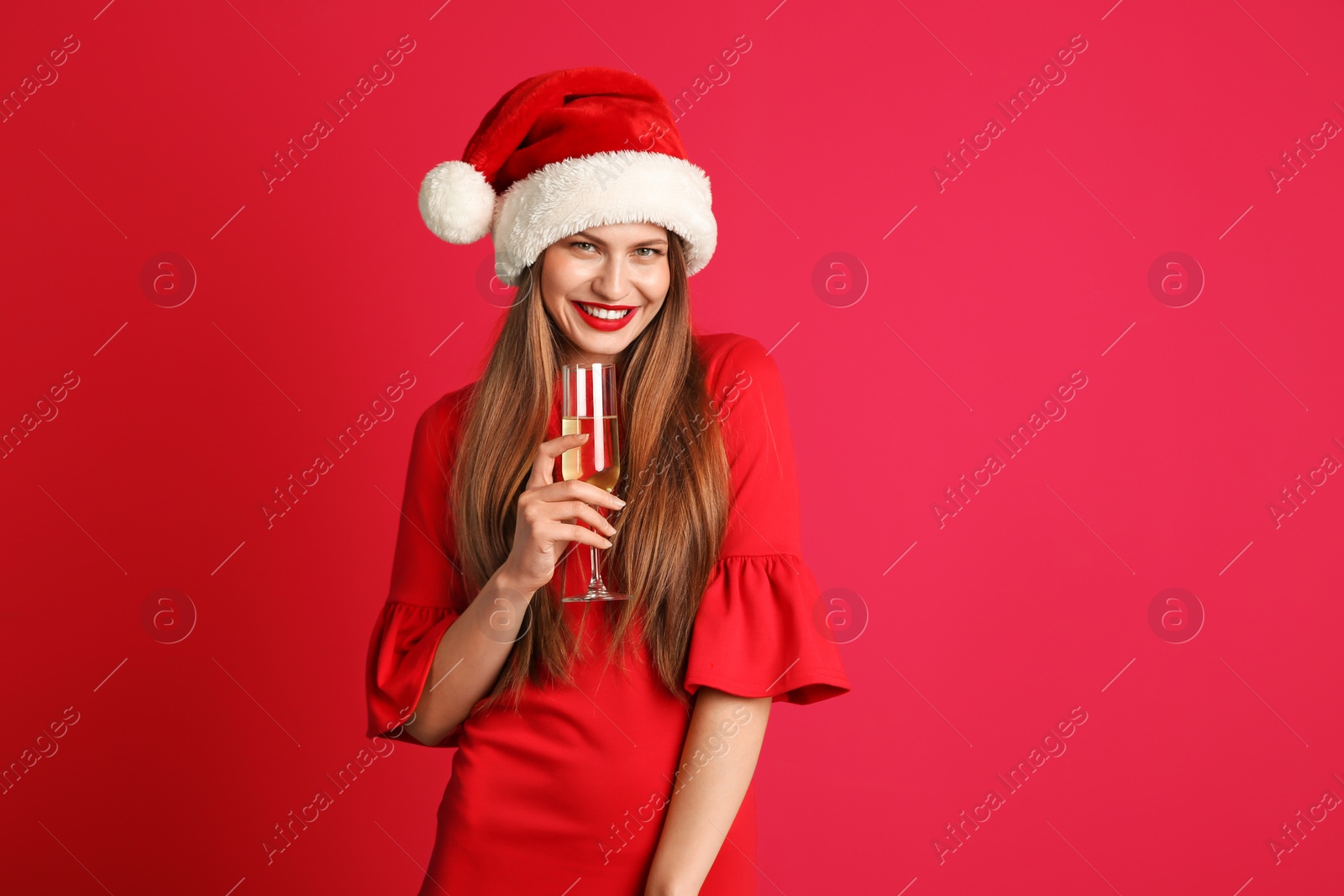 Photo of Young beautiful woman in Santa hat with glass of champagne on color background. Christmas celebration