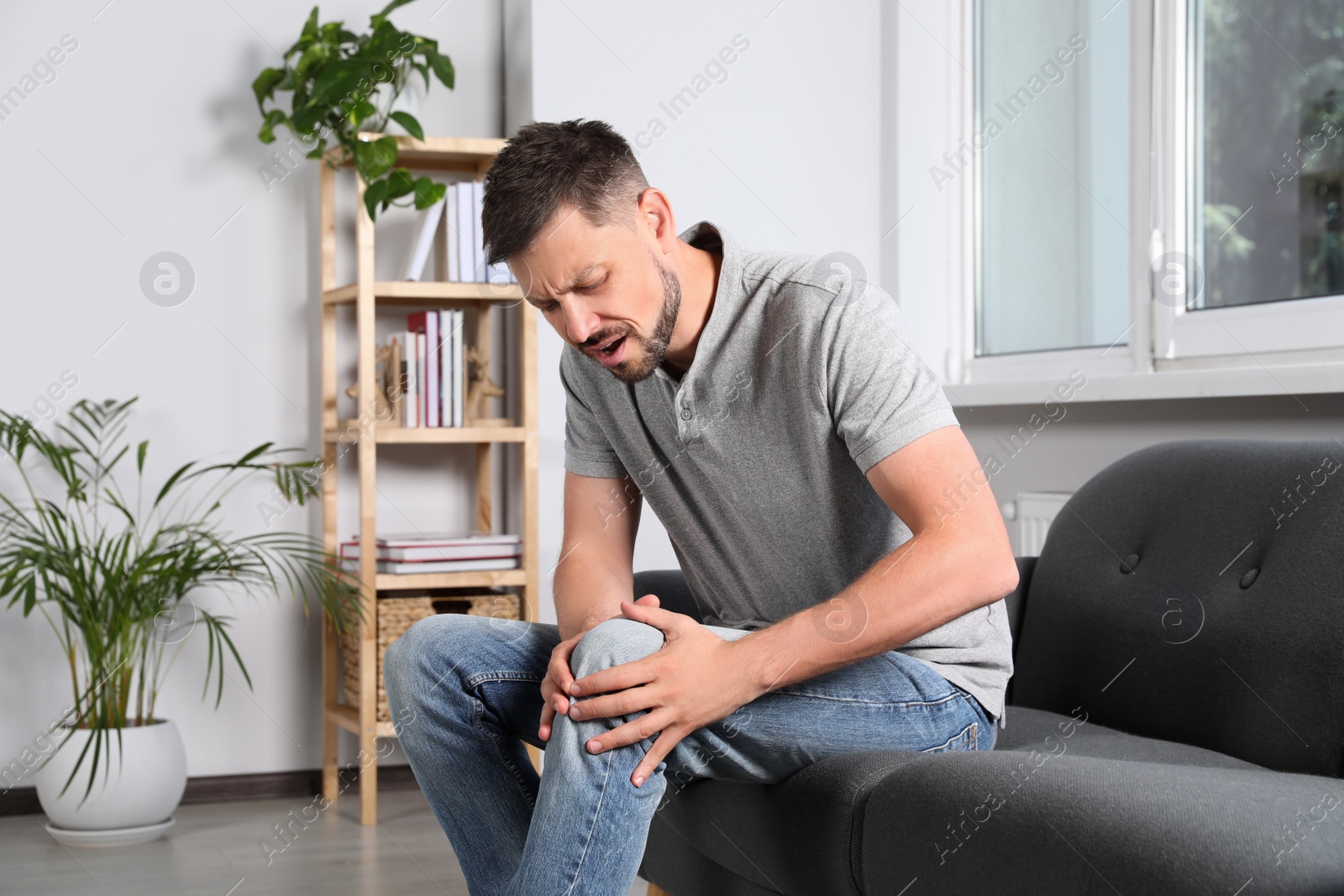 Photo of Man suffering from knee pain on sofa at home