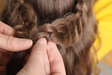 Photo of Professional stylist braiding girl's hair indoors, closeup