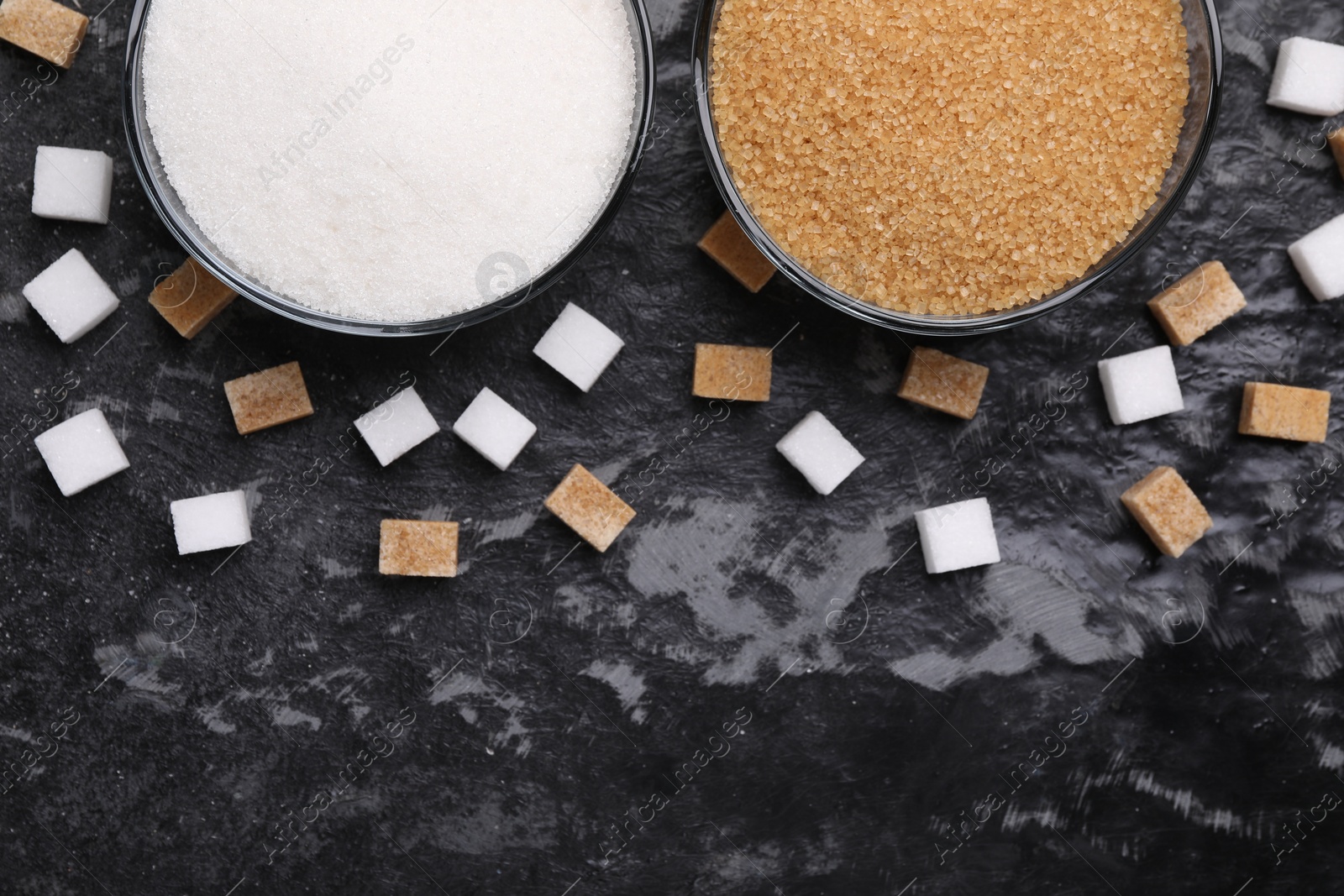 Photo of Different types of sugar in bowls on dark gray textured table, flat lay. Space for text