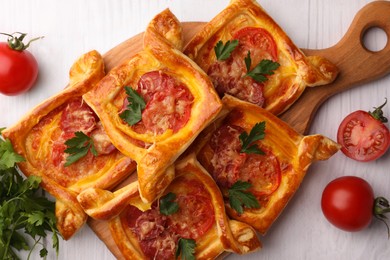 Fresh delicious puff pastry with cheese, tomatoes and parsley on white wooden table, flat lay