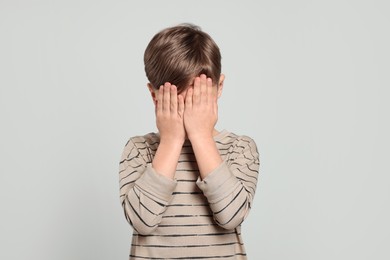 Photo of Boy covering face with hands on light grey background. Children's bullying