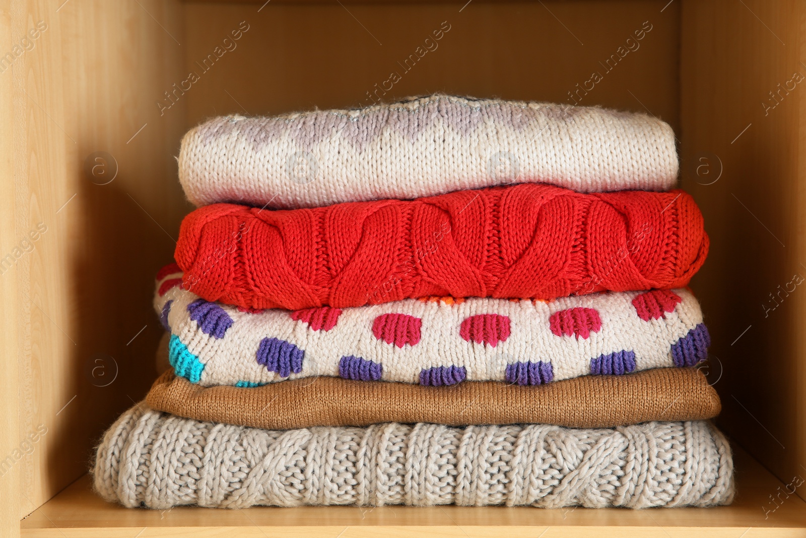 Photo of Stack of folded winter clothes on shelf in wardrobe