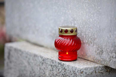 Photo of Candle on light grey granite tombstone outdoors. Funeral ceremony