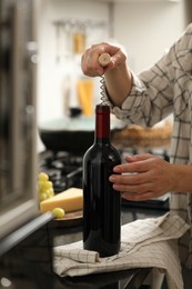 Photo of Woman opening wine bottle with corkscrew at countertop indoors, closeup