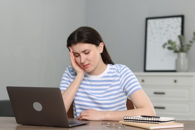 Photo of Overwhelmed woman sitting with laptop at table indoors