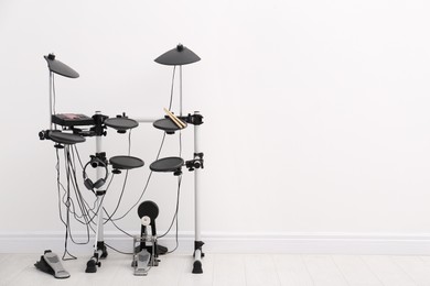 Photo of Modern electronic drum kit near white wall indoors, space for text. Musical instrument