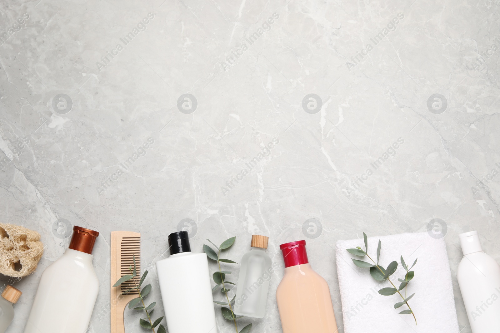 Photo of Shampoo bottles, wooden comb, essential oil, towel, loofah and leaves on white textured table, flat lay. Space for text