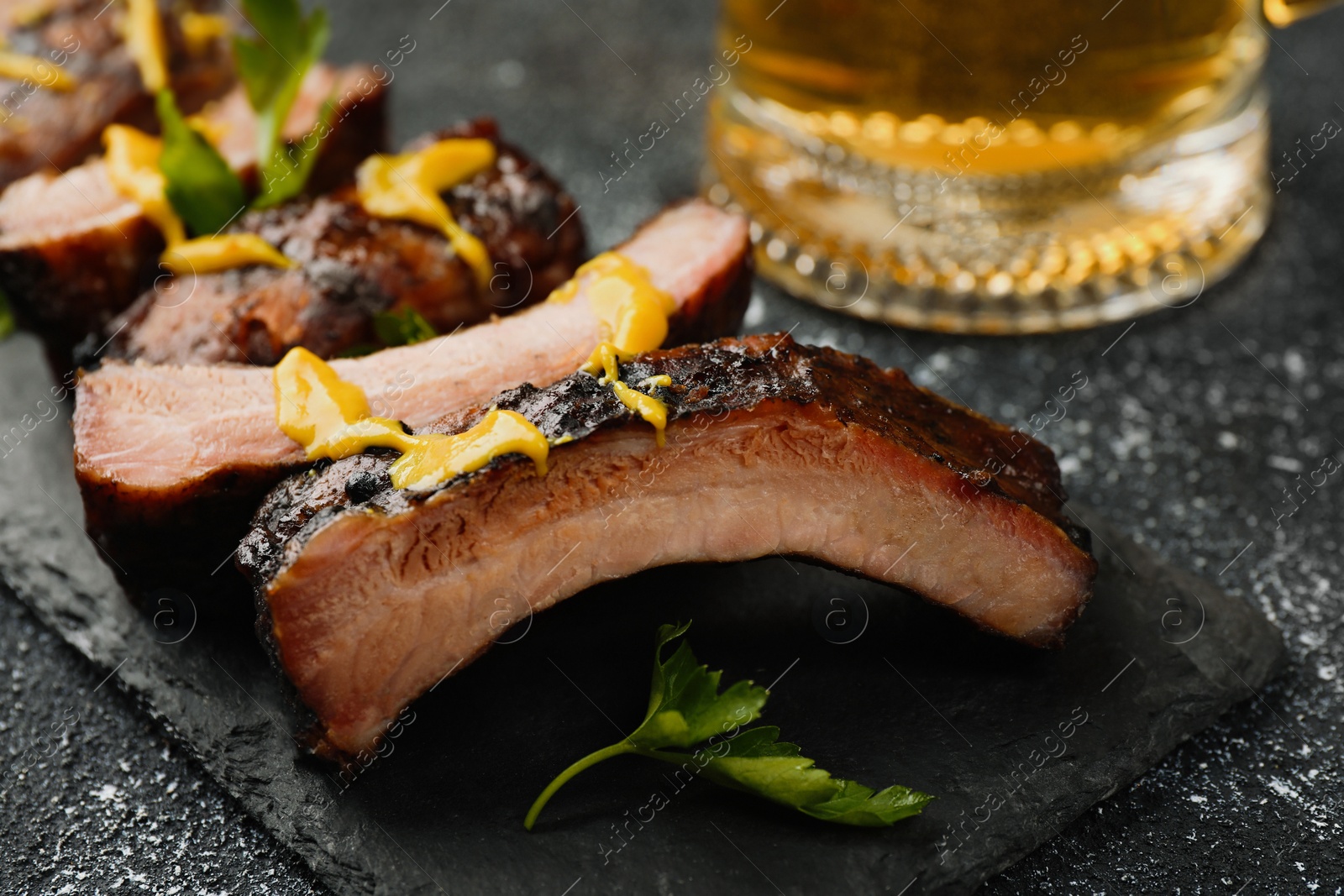 Photo of Delicious grilled ribs on dark grey textured table, closeup