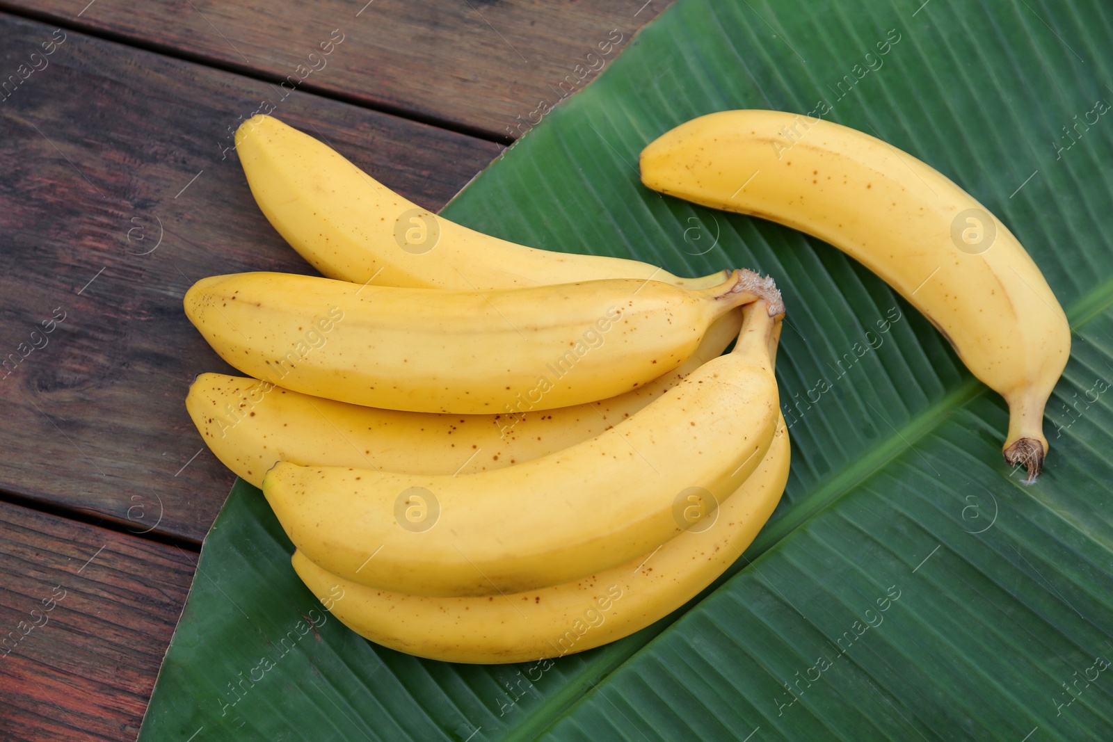 Photo of Delicious bananas and green leaf on wooden table, top view