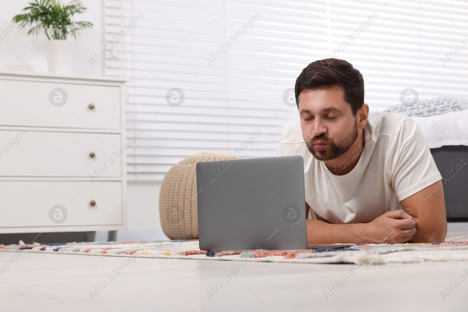 Photo of Man sending air kiss during video chat via laptop at home. Long-distance relationship