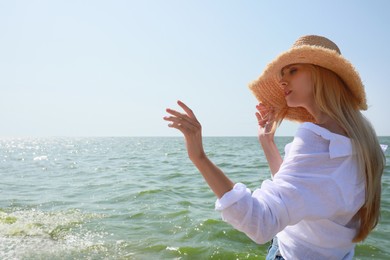 Beautiful young woman with straw hat near sea on sunny day in summer