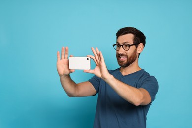 Photo of Handsome man taking photo on smartphone against light blue background