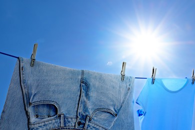 Image of Denim jeans and t-shirt drying on washing line against blue sky