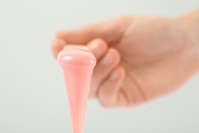 Woman holding spatula with hot depilatory wax on light  background, closeup