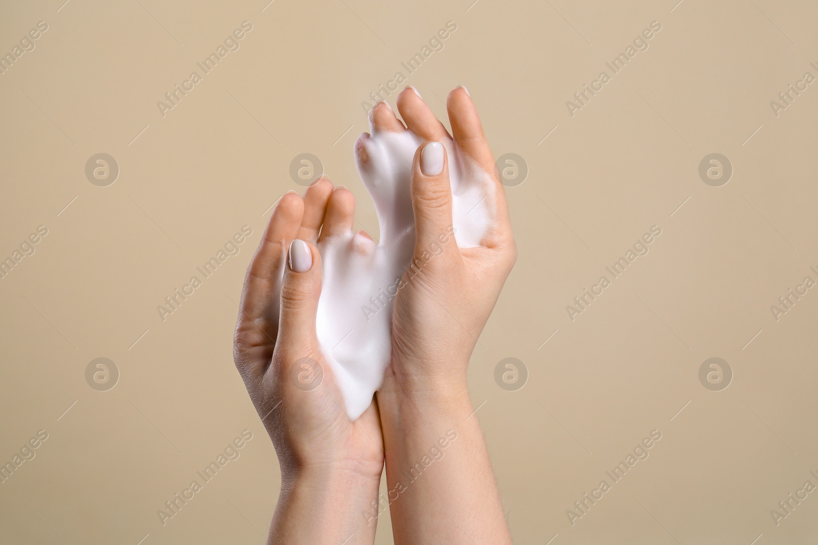 Photo of Woman washing hands with cleansing foam on beige background, closeup. Skin care cosmetic