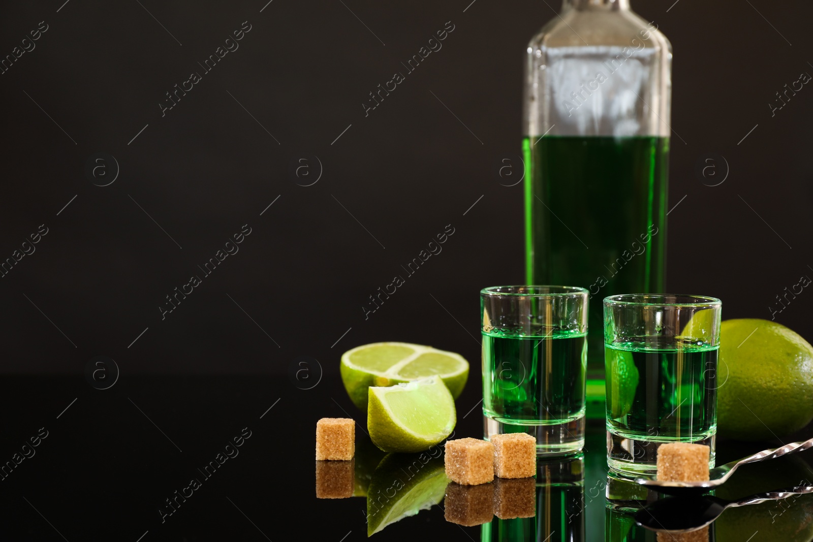 Photo of Absinthe in shot glasses, brown sugar, lime and spoon on mirror table, space for text. Alcoholic drink