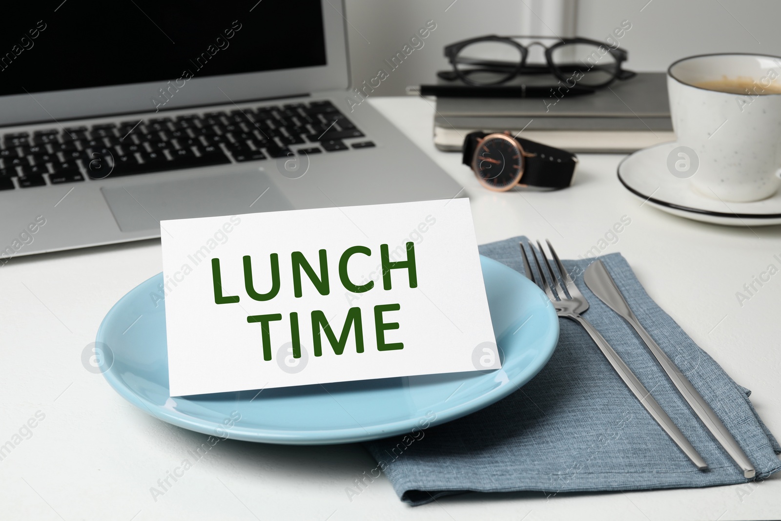 Image of Business lunch. Office desk with plate, cutlery and laptop. Card with phrase Lunch Time on dish