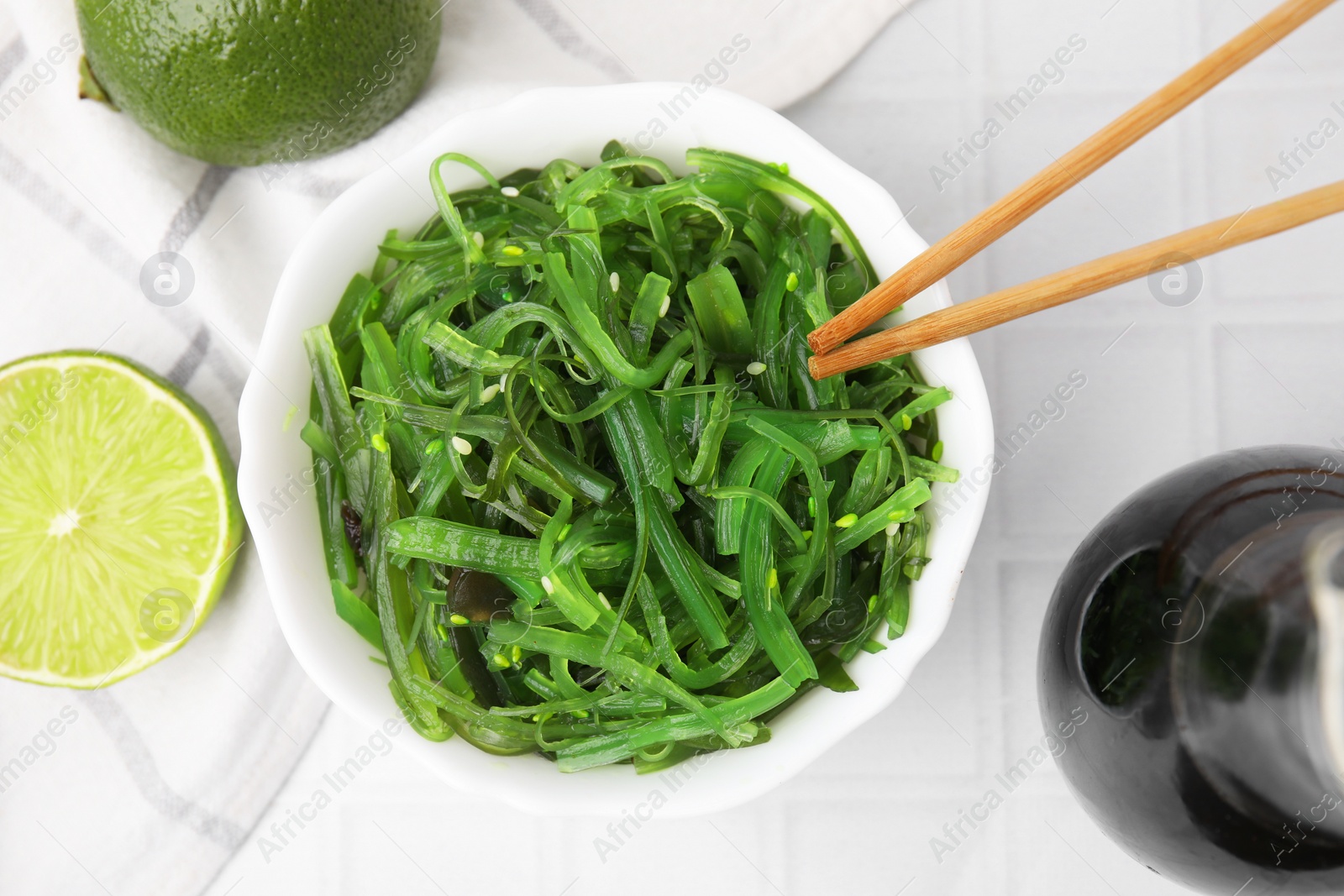 Photo of Tasty seaweed salad in bowl served on white tiled table, flat lay