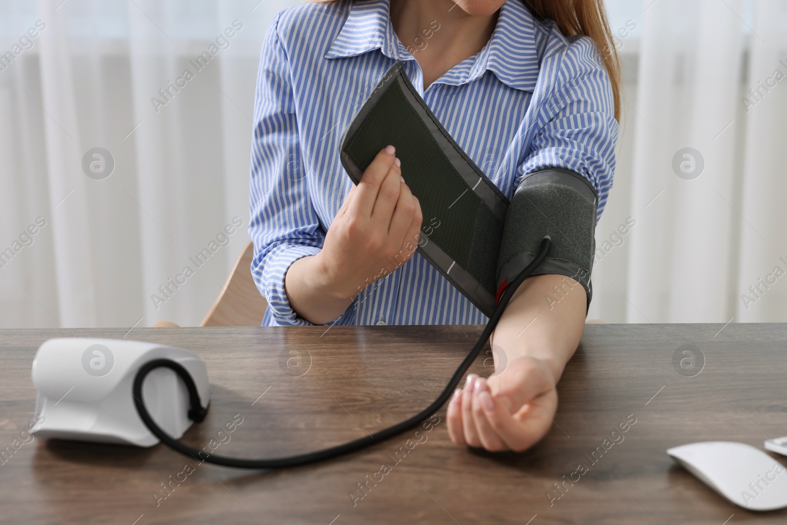 Photo of Woman measuring blood pressure at wooden table in room, closeup