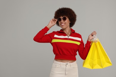 Photo of Happy young woman in stylish sunglasses with shopping bags on grey background