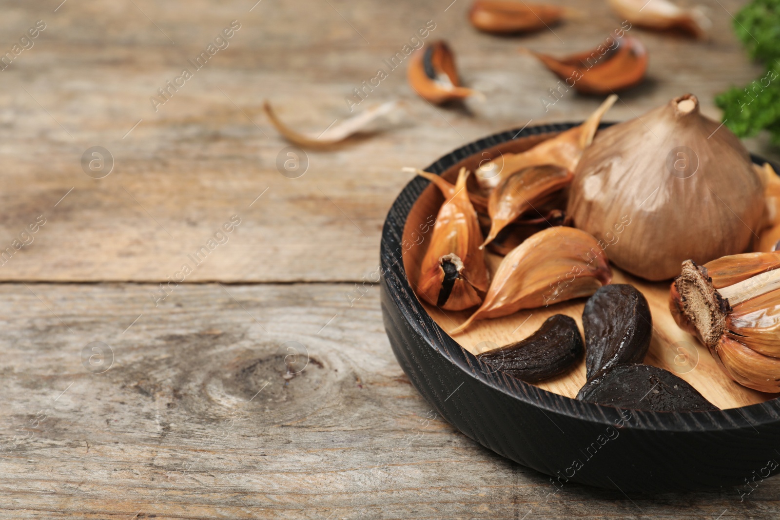 Photo of Bowl with black garlic on wooden table. Space for text