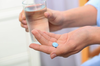 Woman holding pill and glass of water on blurred background, closeup. Space for text