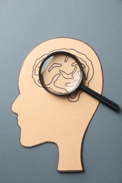 Photo of Amnesia. Human head cutout with drawing of brain and magnifying glass on grey background, top view