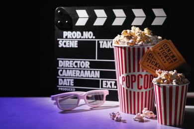 Photo of Delicious popcorn, tickets, glasses and clapper on table