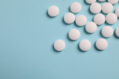Photo of Many white pills on light blue background, flat lay. Space for text