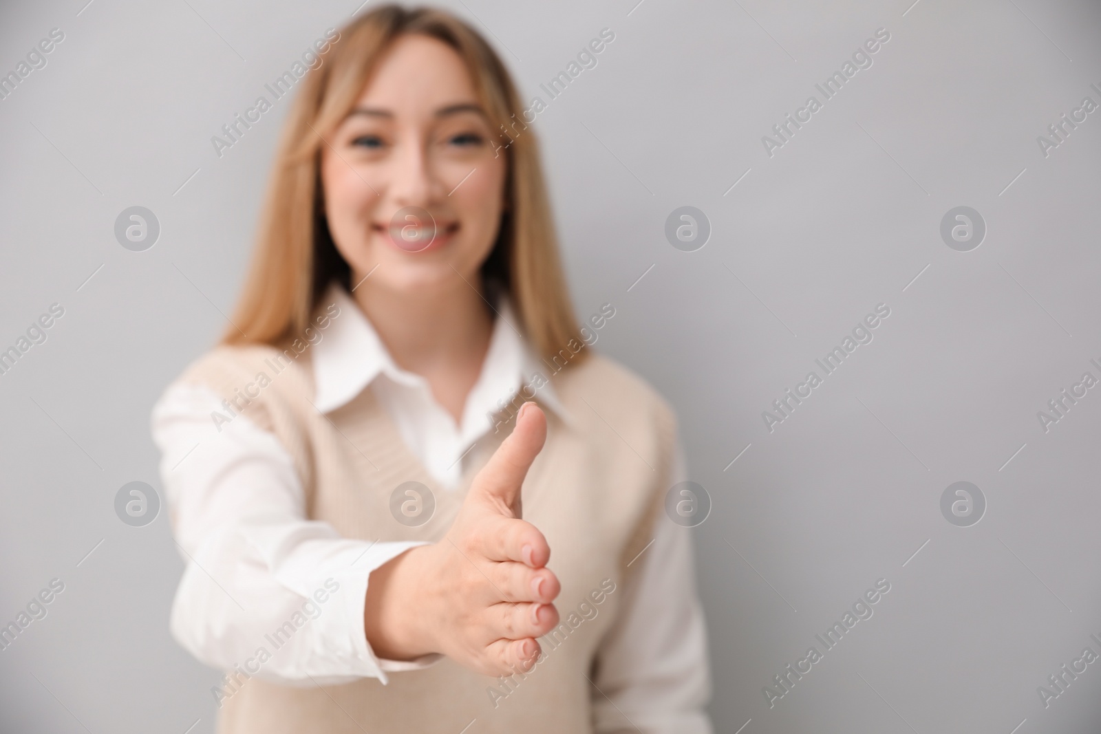 Photo of Happy young woman offering handshake on light grey background. Space for text