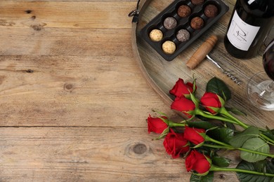 Photo of Red wine, chocolate truffles, corkscrew and roses on wooden table, flat lay. Space for text
